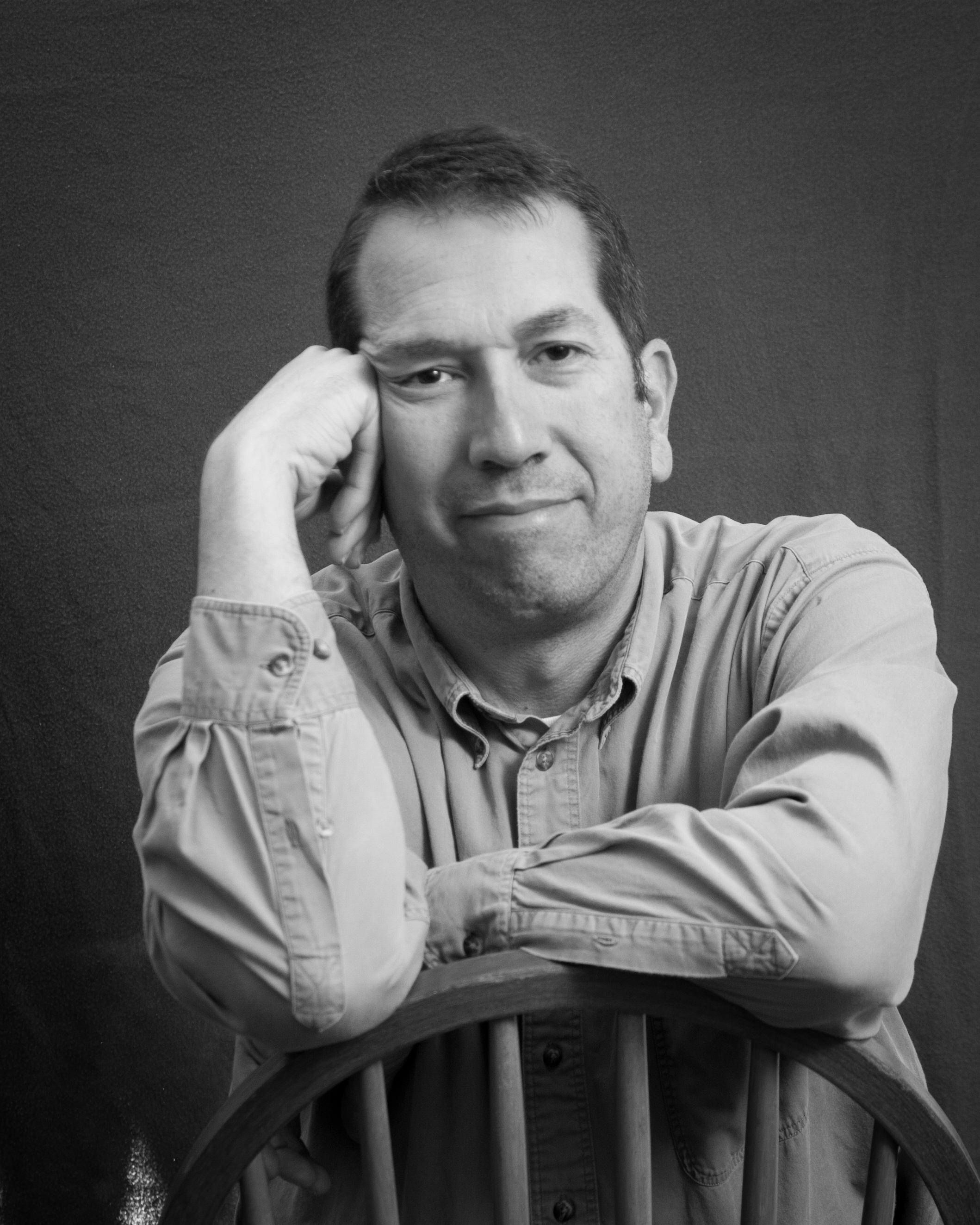 Tall male sitting in a chair smiling.